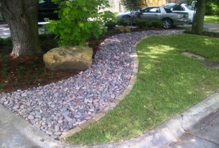 Oklahoma Ledge and Arizona River Rock cascade through the yard with a large Moss Boulder next to the tree.